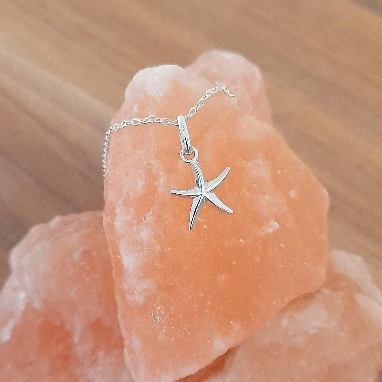 Silver starfish pendant necklace on a pink stone with a blurred wooden background