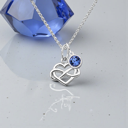 Silver necklace with a heart and infinity symbol pendant featuring a blue gemstone, set against a light gray background.