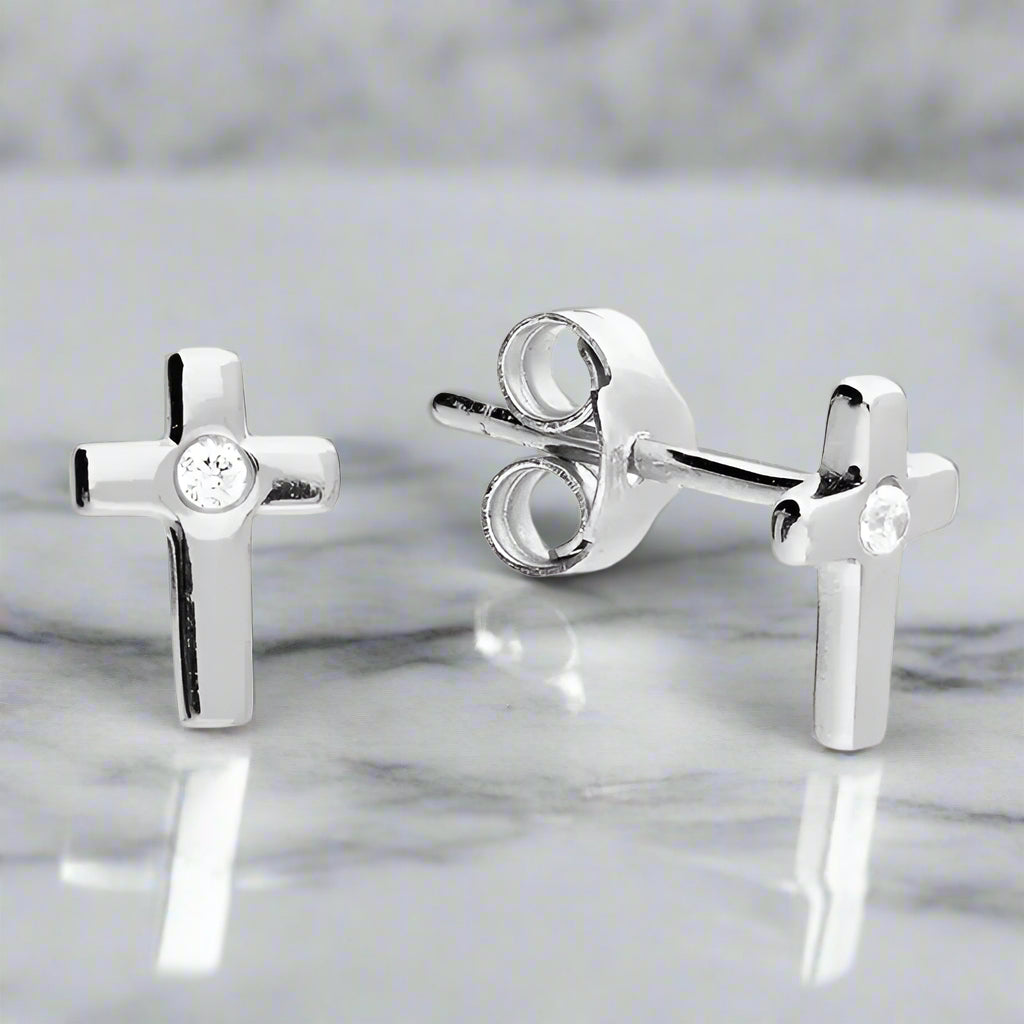 Silver cross-shaped earrings with clear gemstones on a white background