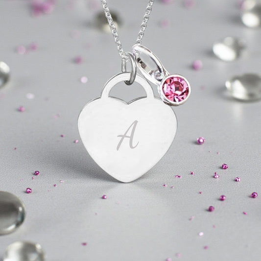 Silver necklace with a heart-shaped pendant and pink gemstone on a gray background with scattered gemstones.