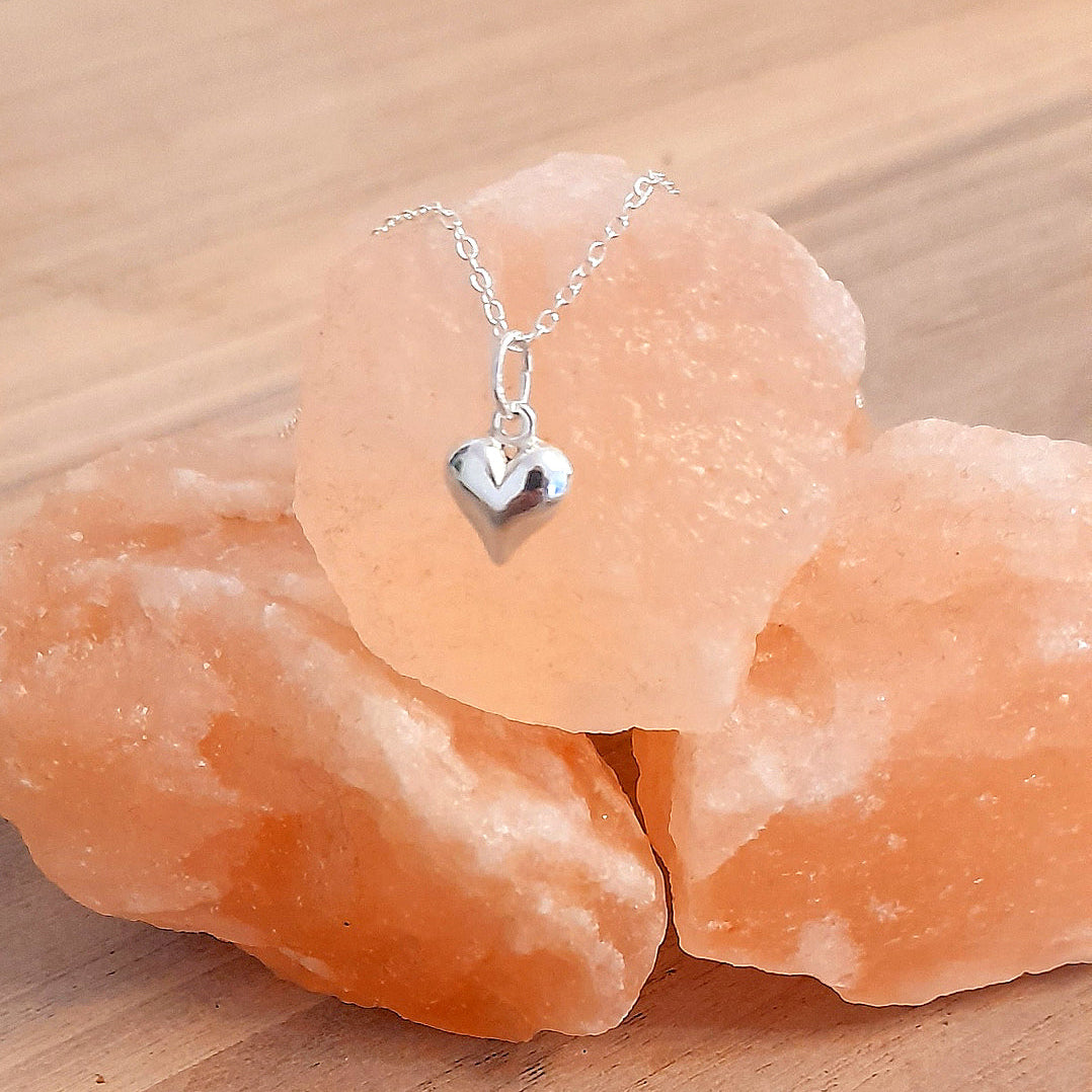 Silver heart-shaped pendant necklace on a piece of pink crystal rock.