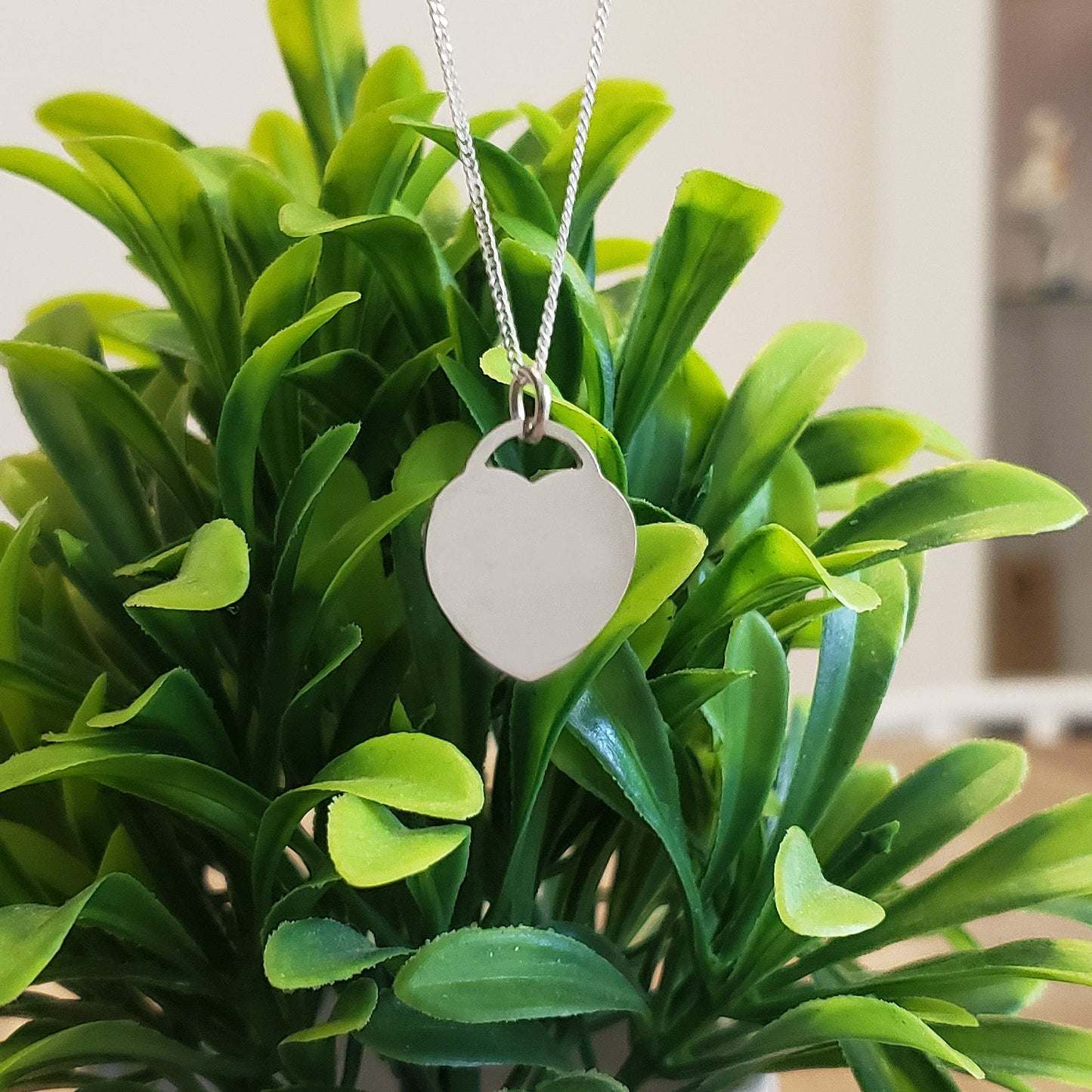Silver necklace with a heart-shaped pendant hanging on a green plant
