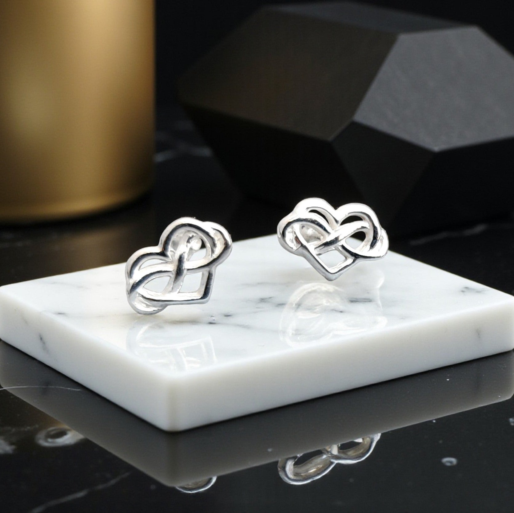 Silver heart-shaped earrings on a marble stand with a dark background