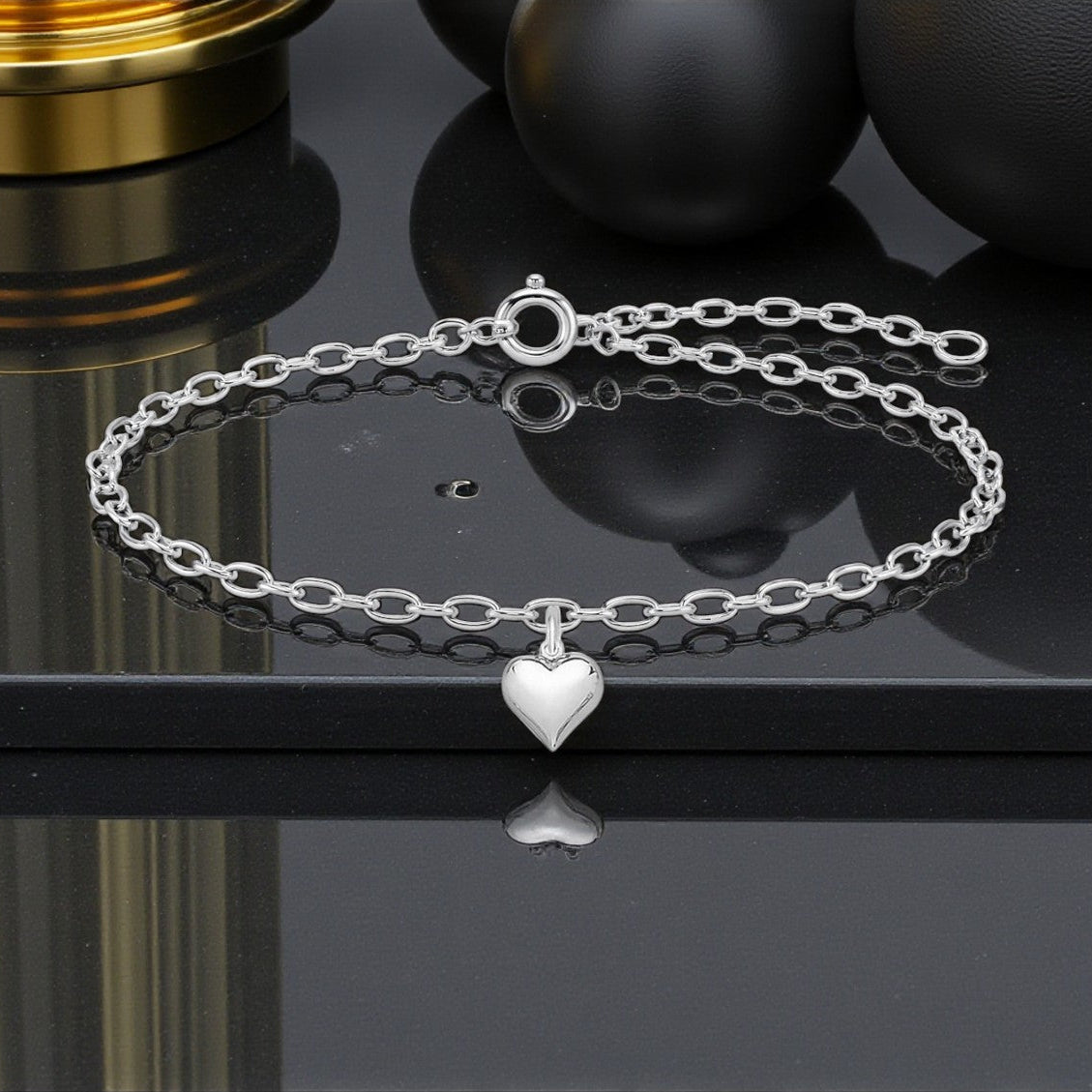Silver bracelet with a heart charm on a reflective black surface