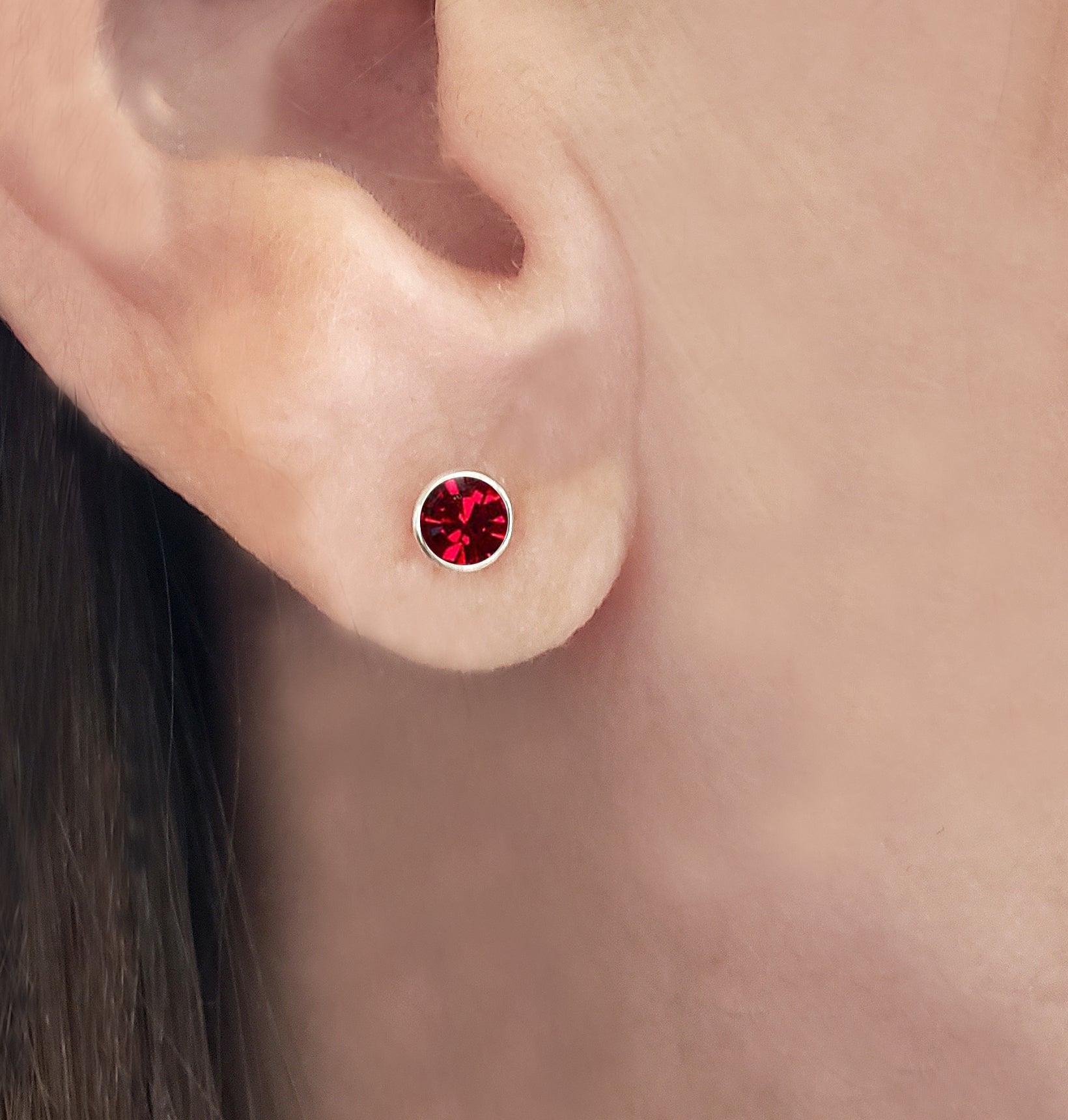 Close-up of an ear wearing a round red gemstone stud earring.