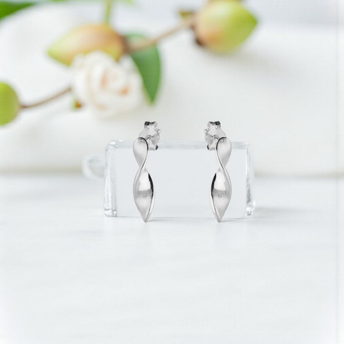Silver earrings on a clear stand with a blurred floral background