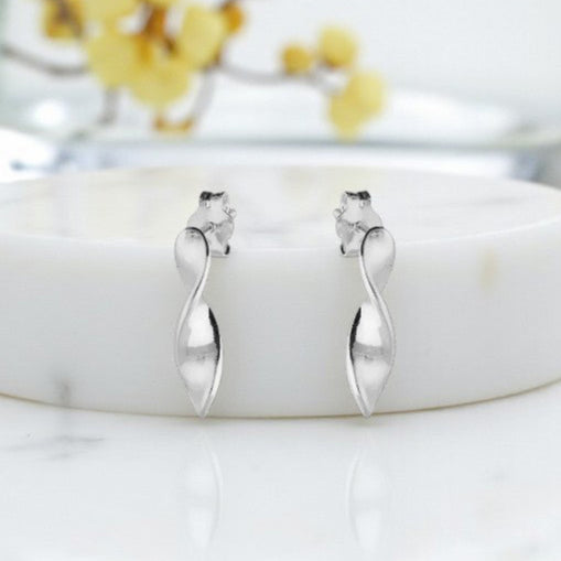 Silver earrings on a white marble surface with a blurred floral background